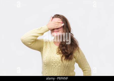 Jolie fille européenne dans chandail jaune fermant les yeux avec la main, ayant l'expression heureuse, attendant de recevoir des présents de son petit ami. Banque D'Images