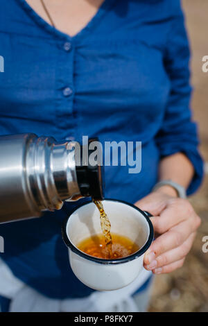 Woman pouring thé chaud d'un thermos sur une plage de sable fin sur une journée ensoleillée. Close up. Banque D'Images