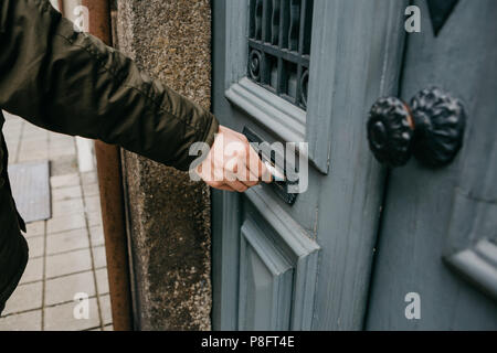 Le facteur met une lettre ou un journal ou magazine dans la boîte aux lettres à la porte d'un bâtiment résidentiel ou d'une personne met une brochure avec de la publicité. Banque D'Images