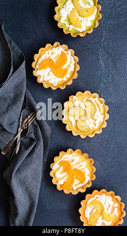 Citron, lime et orange tartelettes décorées avec du yogourt et fruits confits tranches sur un fond texturé bleu. Banque D'Images