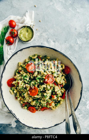 Salade de pâtes à l'avocat végétalien servi la vinaigrette dans un bol blanc céramique faite à la main avec deux cuillères sur le côté. Banque D'Images