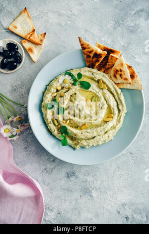 Houmous de haricots blancs crémeux garni d'herbes, l'huile d'olive et pistaches, servi dans un bol bleu clair avec des puces de pita sur le côté. Olives noires, flo printemps Banque D'Images