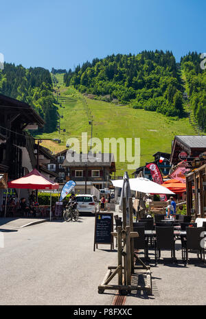 La vue sur la rue Taillle de Mas du Pleneywiith bars boutiques et restaurants avec la télécabine de Pleney et télésiège à Morzine France Banque D'Images