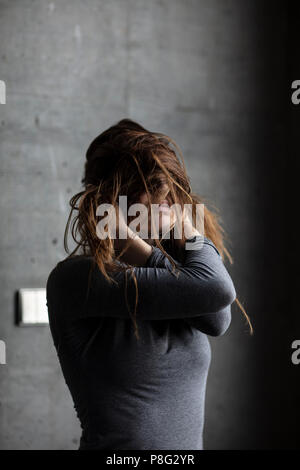 Modèle féminin posant derrière un mur de béton gris obscurcir son visage avec les cheveux. Plan moyen. Banque D'Images