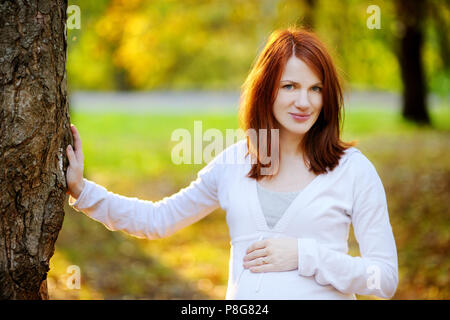 Belle femme enceinte en automne à un coucher de soleil Banque D'Images