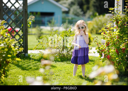 Adorable petite fille aux groseilles rouges dans un jardin Banque D'Images