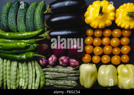 Les concombres, piments, gousses de haricots, petits pois, aubergines, poivrons, tomates jaunes et courges sont disposés en une rangée sur un fond noir Banque D'Images