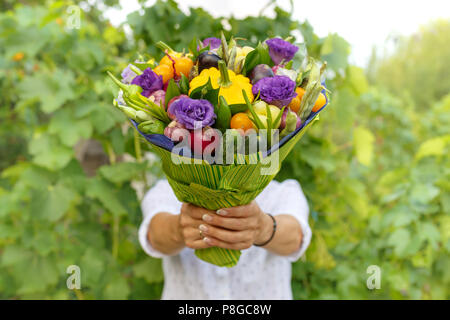 Beau bouquet de légumes frais et de fleurs dans les mains d'une femme comme un cadeau Banque D'Images