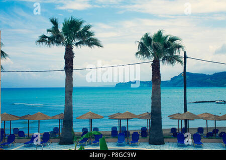 Parasols Palapa rustique et bleu chaises pliantes avec deux palmiers donnant sur la rive de la mer méditerranée et ondulée bleu, Vacances Landsca Banque D'Images
