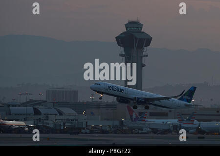 JetBlue Airbus A321 avion de décoller de l'Aéroport International de Los Angeles, LAX, au lever du soleil, la tour de contrôle de l'ATC derrière. Banque D'Images