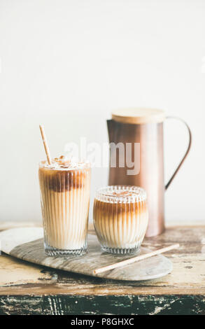 Café glacé dans de grands verres avec du lait et des pailles à bord sur table en bois rustique, mur blanc et verseuse à fond, l'espace de copie. Être rafraîchissant d'été Banque D'Images