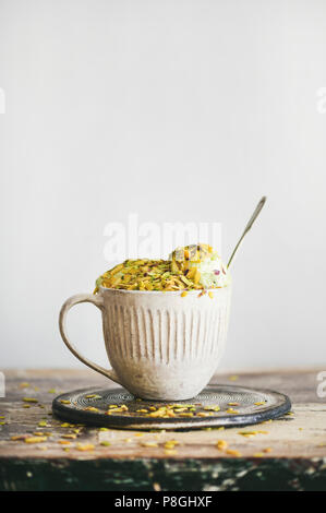 Glace Pistache maison tasse en céramique en vert avec les pistaches sur table en bois rustique, composition verticale, l'espace de copie. Glace rafraîchissante de l'été Banque D'Images