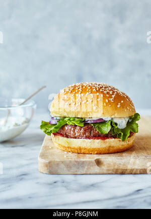 Hamburger d'agneau au pain brioché avec du yaourt à la menthe, servi sur une planche en bois Banque D'Images