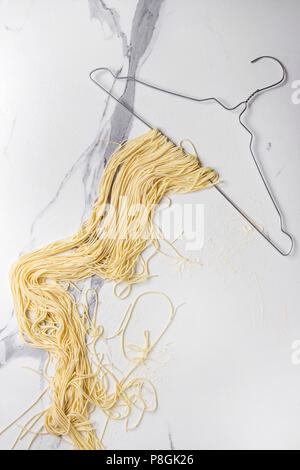 Spaghetti italienne maison Pâtes alimentaires non séché sur un cintre sur le marbre blanc texture background. Mise à plat, de l'espace. Banque D'Images