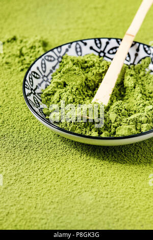 Le thé vert matcha en poudre dans un bol en céramique avec cuillère bambou traditionnel plus de poudre matcha comme arrière-plan. Banque D'Images