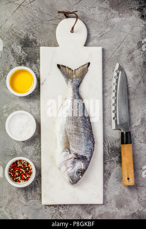 De délicieux poissons daurade fraîche sur du marbre, fines herbes et épices sur fond noir en gris. Concept de cuisine Banque D'Images