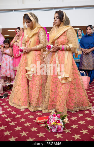 Deux femmes en robes identiques à une cérémonie de mariage dans le temple à la Sikh Society à Richmond Hill, Queens, New York. Banque D'Images