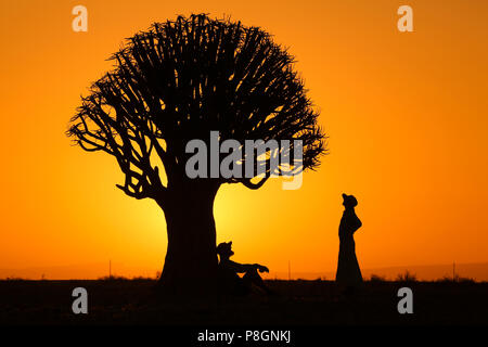 Silhouette d'un baobab avec homme et femme se reposant au coucher du soleil avec une lueur dorée. Banque D'Images