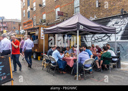 Un groupe diversifié de la population locale et les travailleurs de manger des aliments de rue à proximité de cale dans le jupon Lane Market, Tower Hamlets, East End, Londres, Banque D'Images