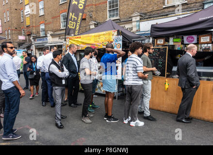 Les résidents locaux et les travailleurs en attente à deux stands de nourriture de rue dans le jupon Lane Market, Tower Hamlets, London, England, UK Banque D'Images