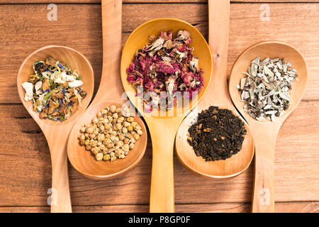 Cuillères en bois avec différentes herbes pour perfusion, style rustique, sur fond de bois. Banque D'Images