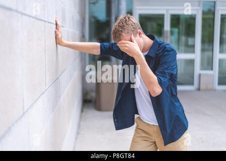 Des ados en colère appuyé contre un mur de brique à l'extérieur d'un bâtiment public. Banque D'Images