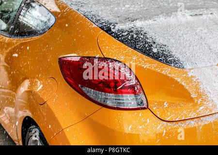 Voiture jaune fenêtre arrière entièrement recouvert d'une épaisse couche de mousse de shampooing blanc, au lavage en lave-auto. Banque D'Images