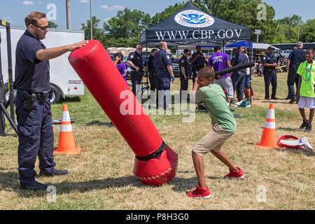 Detroit, Michigan, USA - 11 juillet 2018 - Les agents de l'US Customs and Border Protection encouragent les jeunes à battre un sac de frappe à taille humaine avec une matraque. Le bureau a encouragé l'action de continuer même après le sac était allongé sur le sol. CBP avait un stand à la Journée annuelle de la jeunesse métropolitaine de Detroit, qui attire des milliers d'enfants des écoles pour une journée de l'alimentation, des jeux, des démonstrations, et d'autres activités. Crédit : Jim West/Alamy Live News Banque D'Images