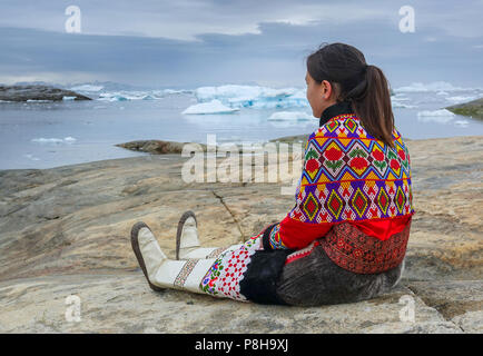 21.06.2018, Gronland, Danemark : Une jeune femme en costume national le 21 juillet est assis sur un rocher dans la ville côtière de Ilulissat dans l'ouest du Groenland. La ville est située sur le fjord glacé d'Ilulissat, qui est connu pour ses icebergs particulièrement grande dans la baie de Disko. Photo : Patrick Pleul/dpa-Zentralbild/ZB | conditions dans le monde entier Banque D'Images