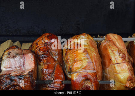 Close up plusieurs gros morceaux de jambon de porc en rotation de la viande d'être uniformément grillés sur feu de bois ouvert brochette, high angle view Banque D'Images