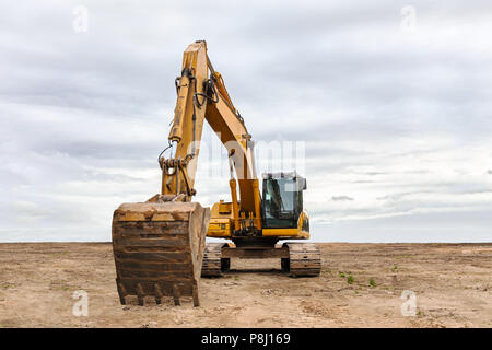 Excavatrice jaune lourd avec pelleteuse stationnée sur le site de construction contre ciel dramatique Banque D'Images