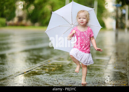 Cute little girl debout dans une flaque d'holding umbrella sur un jour d'été pluvieux Banque D'Images