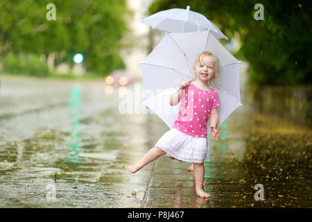 Cute little girl debout dans une flaque d'holding umbrella sur un jour d'été pluvieux Banque D'Images