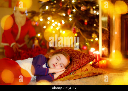 Adorable petite fille dormir sous l'arbre de Noël par une cheminée la veille de Noël Banque D'Images