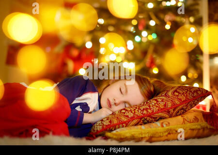 Adorable petite fille dormir sous l'arbre de Noël par une cheminée la veille de Noël Banque D'Images