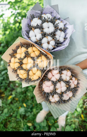 Trois belles et bouquets différents avec lavande en coton femme mains . fleurs couleur lilas. placé dans un sac de papier coloré de fleurs. mélange de couleurs. Banque D'Images