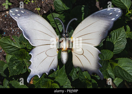 Plastique blanc fake butterfly entre plantes vertes dans le jardin Banque D'Images