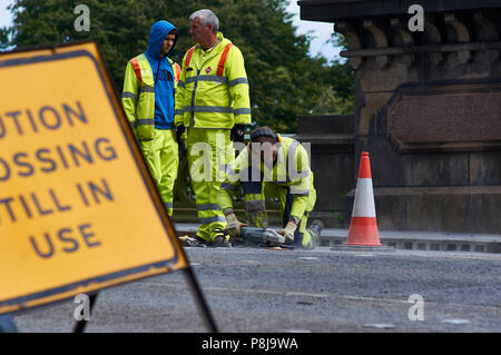 Un travailleur d'entretien des routes à l'aide d'une meuleuse d'angle power tool pour terminer la route réparations de surface. Travailleur est le port de protège-oreilles et des vis de haut. Banque D'Images
