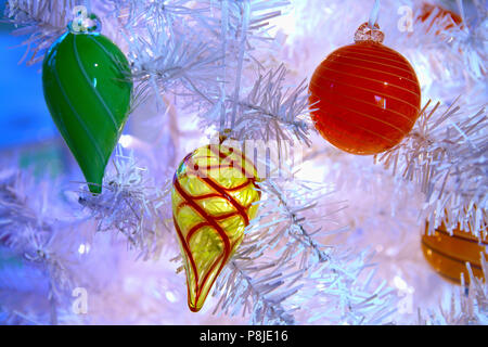 Décorations en verre soufflé blanc suspendu à un arbre de Noël avec des lumières scintillent enfilés dans tout. Banque D'Images