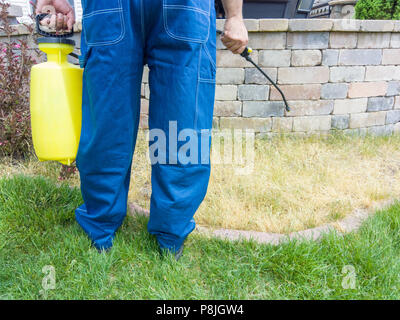 Pulvérisation jardinier un patch d'herbe avec les herbicides à l'aide d'un pulvérisateur portatif vue libre montrant ses jambes, les mains et l'équipement Banque D'Images