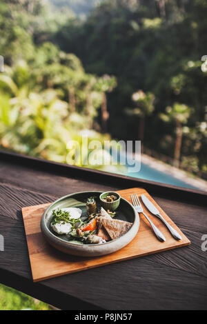 Petit-déjeuner de l'est avec les oeufs pochés, tomates, couscous, aubergines et sauce épicée dans une plaque en céramique sur un support en bois Banque D'Images