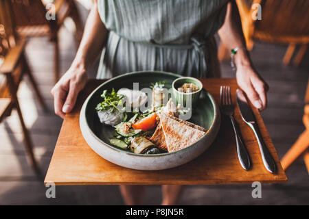 Femme mains tenant la plaque avec petit-déjeuner oriental avec des œufs pochés, des tomates, du couscous, des aubergines et sauce épicée sur un support en bois Banque D'Images