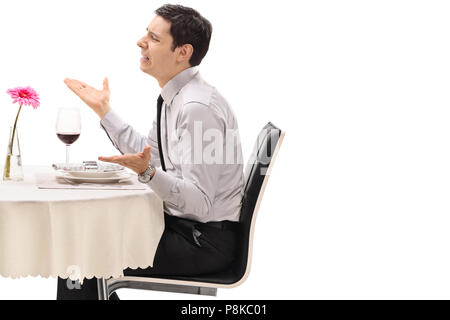 Colère jeune homme assis à une table de restaurant isolé sur fond blanc Banque D'Images