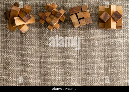 Quatre différents puzzles en bois disposés en ligne comme une frontière sur un tissu marron clair ou lin contexte with copy space Banque D'Images