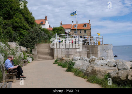 Vue de mur du port à Robin Hood's Bay,Yorkshire,Angleterre,Heritage Coast UK de la promenade menant à la plage de rochers avec people relaxing Banque D'Images