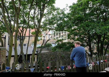 L'homme se reposant sur clôture avec dos à la caméra et à l'ensemble de flux en centre de Robin Hood's Bay,Patrimoine,Angleterre Yorkshire Coast,UK Banque D'Images