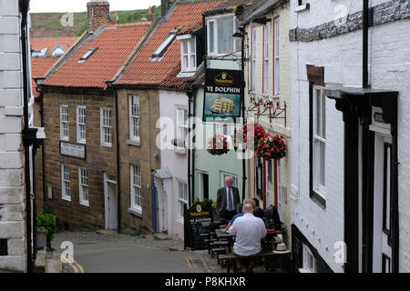 Vue de la rue King, Robin Hood's Bay,Yorkshire,Angleterre,Heritage Coast UK avec Ye Dolphin House public à droite et deux hommes à l'extérieur dans la rue Banque D'Images