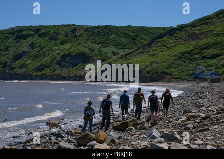 Les vacanciers et les personnes à pied les rochers sur la plage avec un chien par la mer à Runswick Bay, North Yorkshire Heritage Coast. Banque D'Images