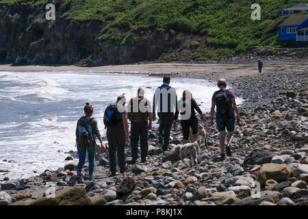 Les vacanciers et les personnes à pied les rochers sur la plage avec un chien par la mer à Runswick Bay, North Yorkshire Heritage Coast. Banque D'Images