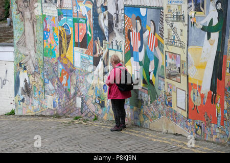 Personnes âgées,pensionné lady en utilisant téléphone contre l'art de rue, graffiti sur un mur de la rue pavée Blands Falaise, Yorkshire holiday resort de Scarborough,UK Banque D'Images